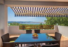 Un patio techado al aire libre con una mesa y sillas, vista al paisaje y una barandilla.