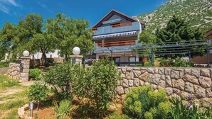 A modern two-story building with a stone wall in front, surrounded by greenery and trees. - Apartments Ivni (Karlobag)