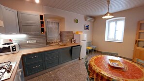 A compact kitchen with a central island, a dining area with a round table, and a window providing natural light. - Apartment Nadi (Mali Losinj)