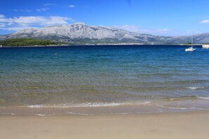 En strand med klart vand, en sejlbåd og et bjerg i baggrunden.