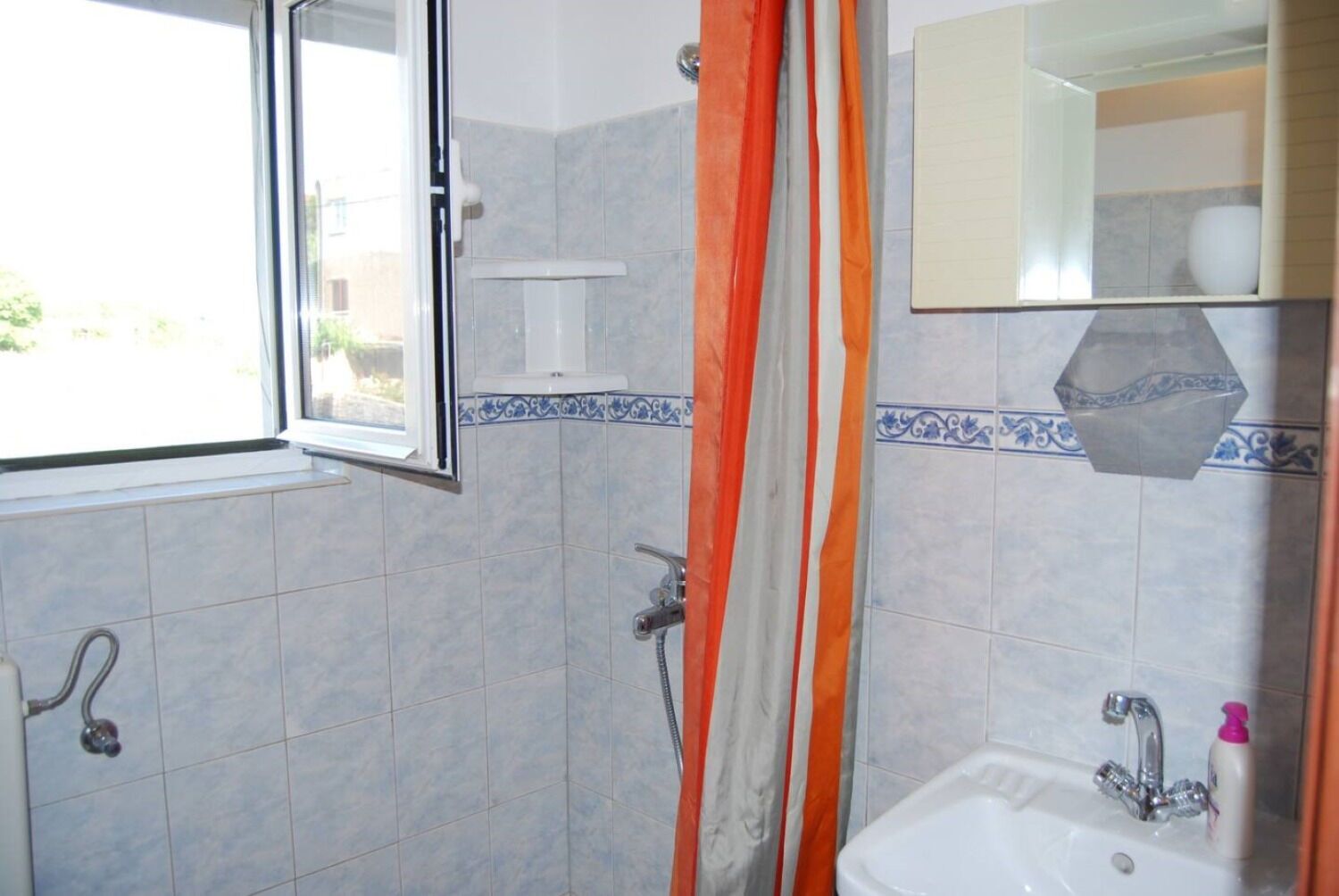A bathroom with a shower, a sink, and a window.