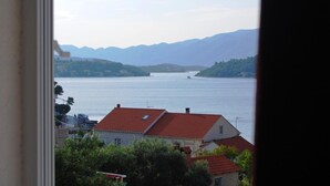 Blick auf die Küste mit einem Haus mit rotem Dach, einem Gewässer und fernen Bergen.