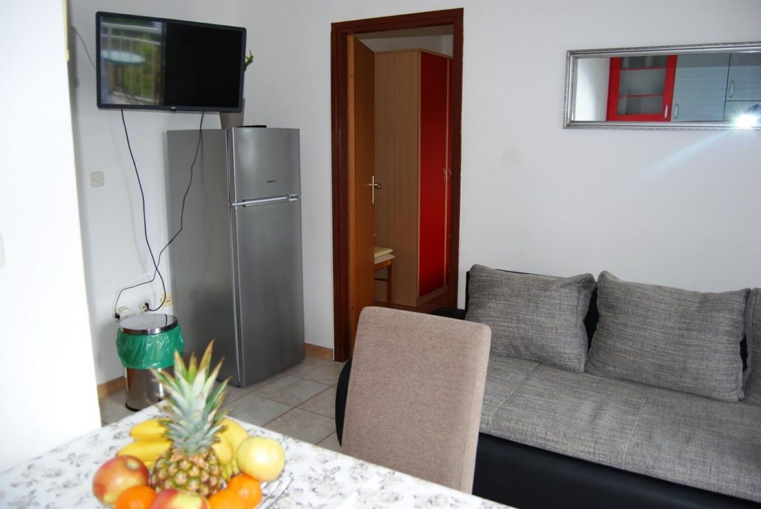 A compact living space with a kitchenette, a grey sofa, and a fruit bowl on the table.
