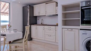 Cozinha compacta com armários brancos, máquina de lavar embutida e área de refeições com mesa e cadeiras.