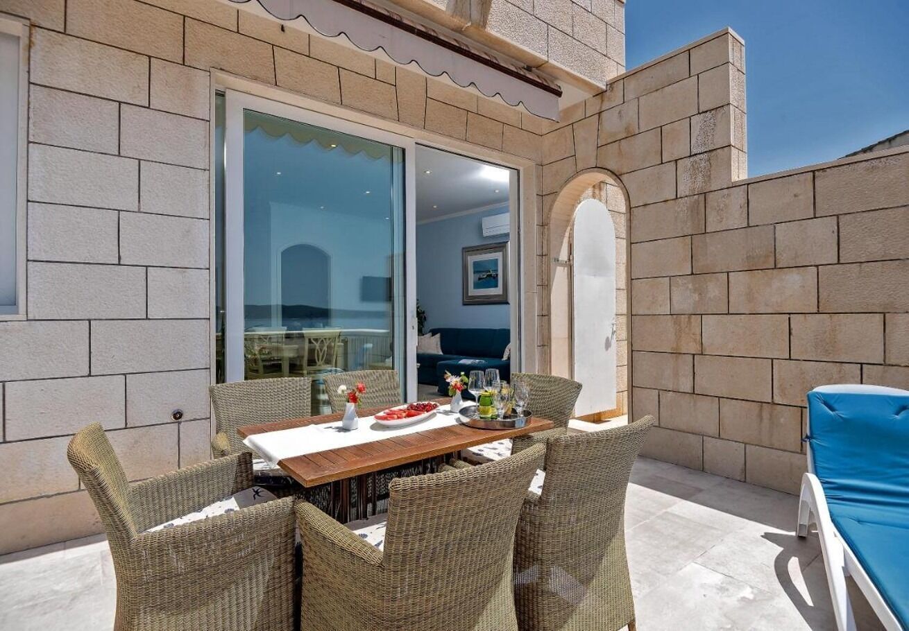 An outdoor patio with a wooden table and wicker chairs, a blue lounge chair, and a stone wall.