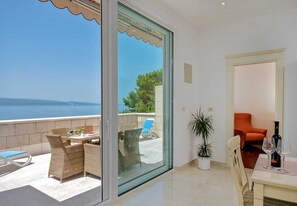 A balcony with wicker furniture and a table, a potted plant, and a view of the sea. - Apartments Draga (Brela)