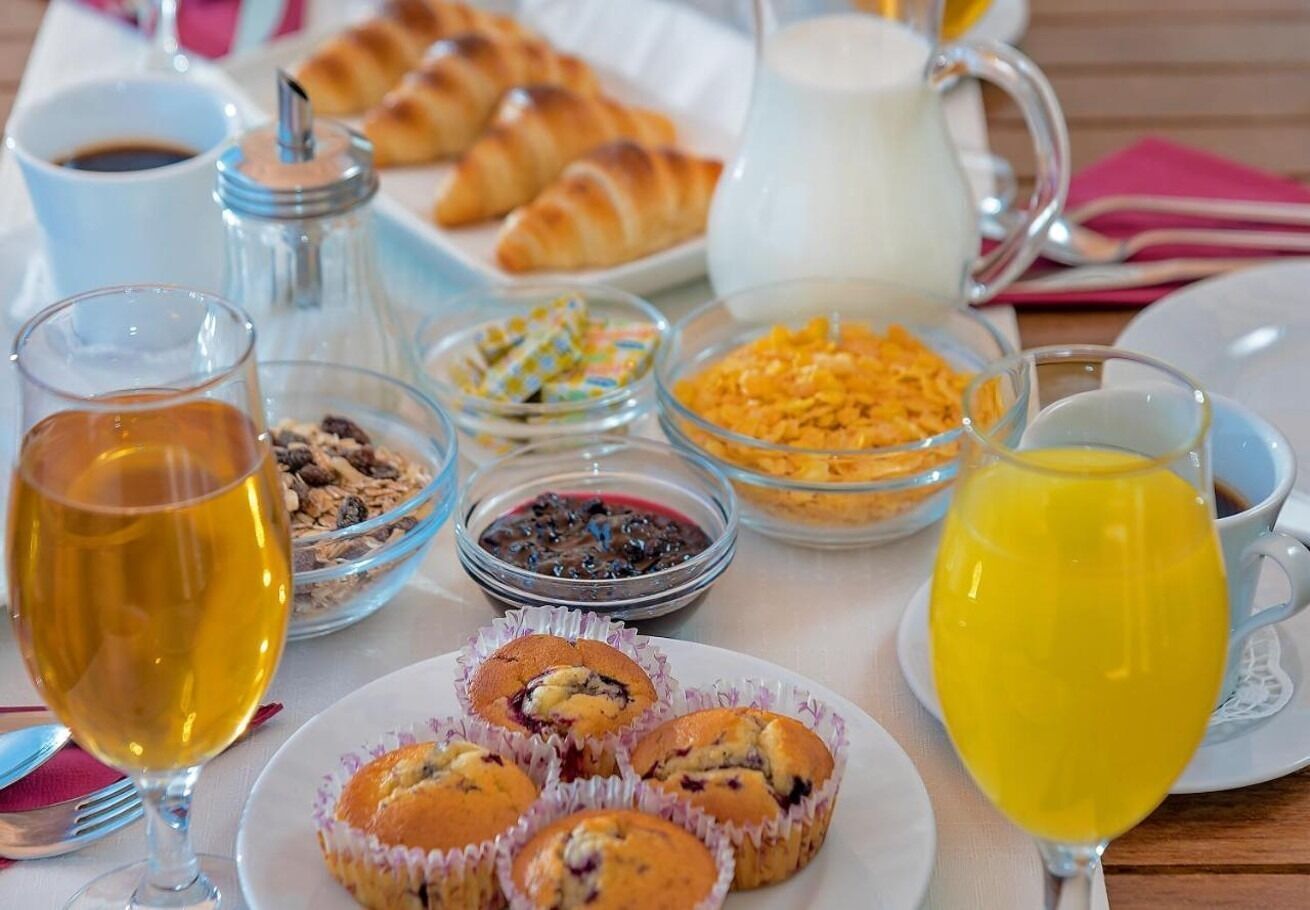 Une table de petit-déjeuner avec des muffins, des céréales, du jus de fruits, du café et des croissants.