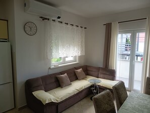 A living room with a brown sofa, a glass coffee table, a wall clock, and a window with curtains. - Apartment Mira (Rab)