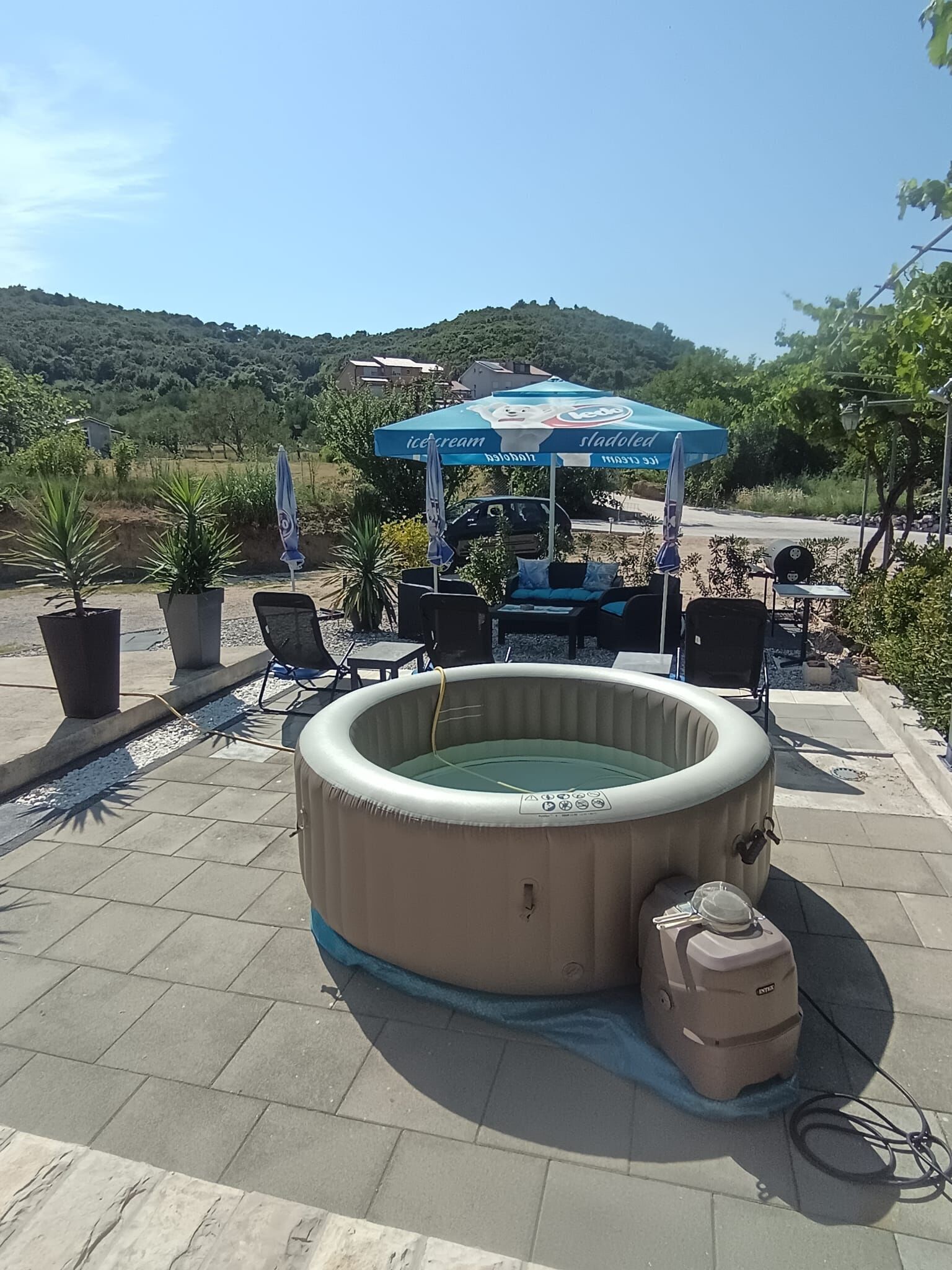 Une piscine extérieure avec des chaises longues, un barbecue et un espace ombragé équipé d’un parasol.