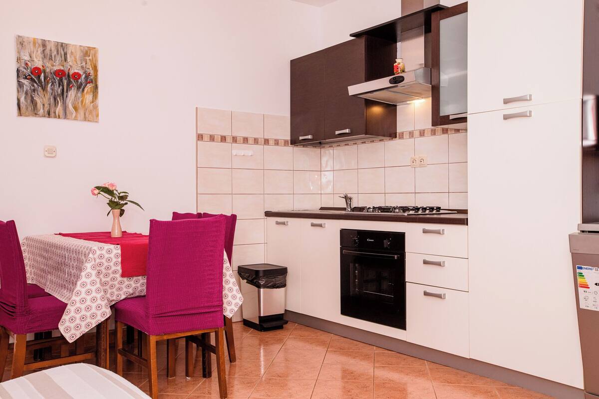 A kitchen with white cabinets, a black oven, and a dining table with pink chairs.