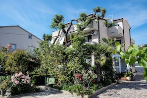 A multi-story building with a garden in front, a satellite dish, and a paved pathway. - Apartments Zdenka (Rab)