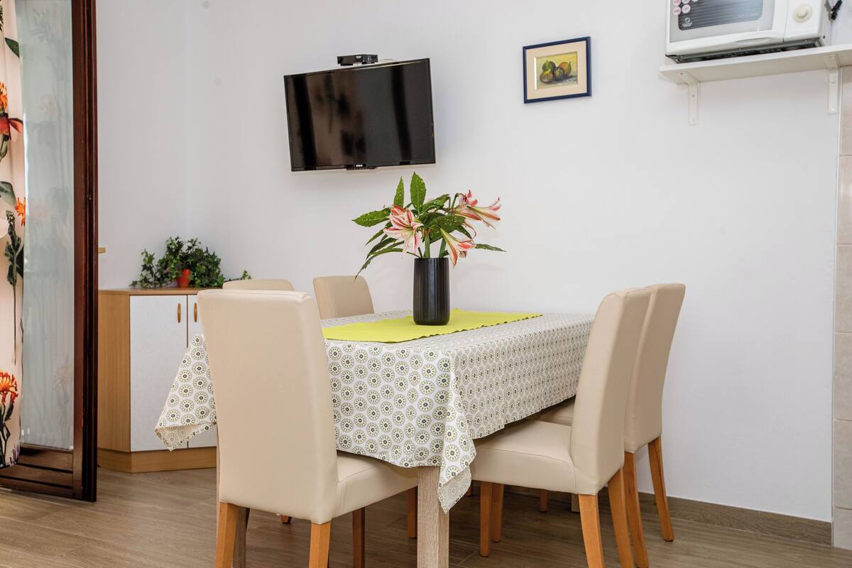 A dining area with a table set for four, a TV mounted on the wall, and a microwave above the table.
