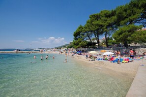 Una playa con agua cristalina, gente nadando y tomando el sol, y árboles a lo largo de la orilla.