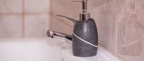A bathroom with a marble wall, a white sink, and a black soap dispenser.