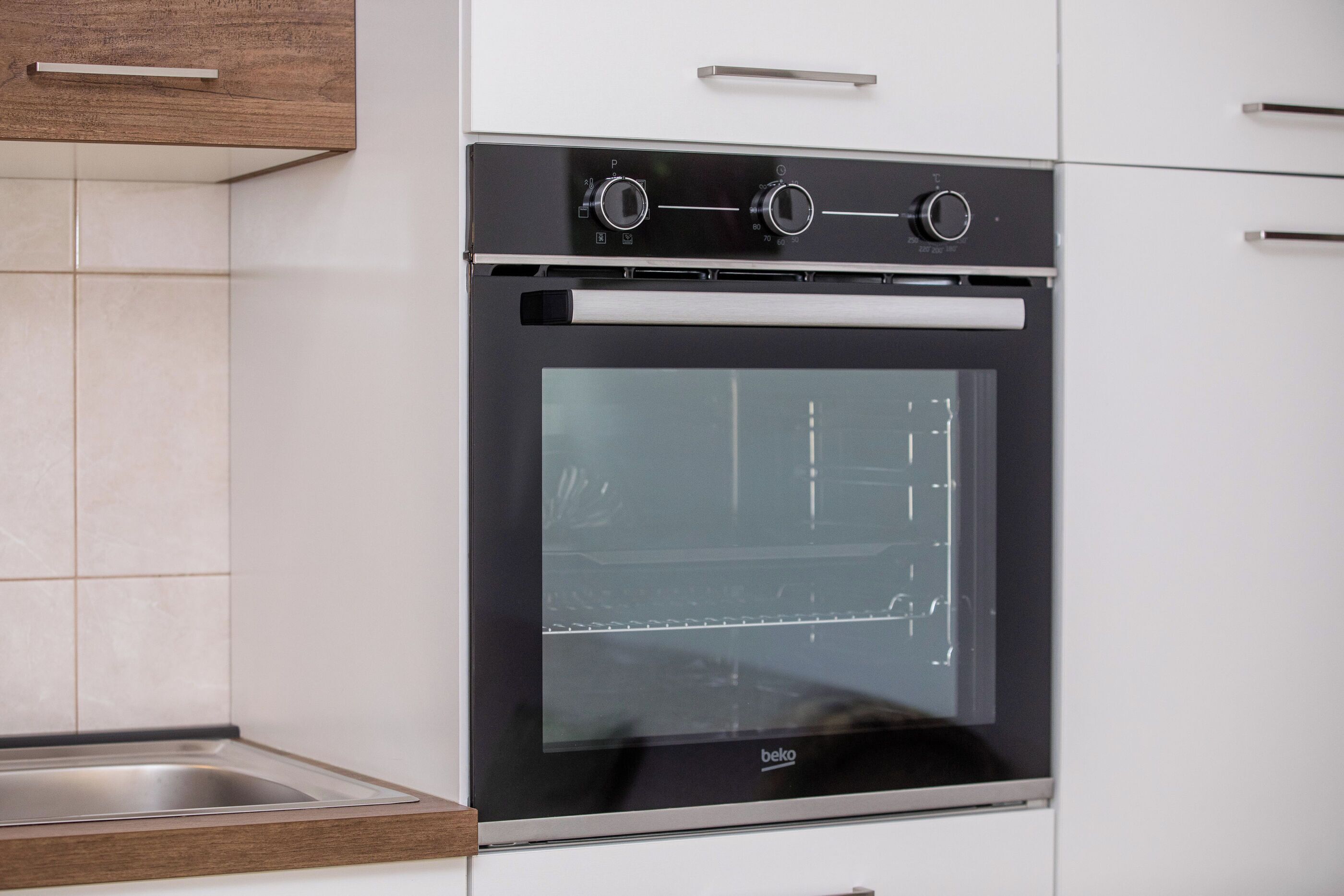 A modern kitchen with a built-in oven, stainless steel sink, and wooden cabinetry.