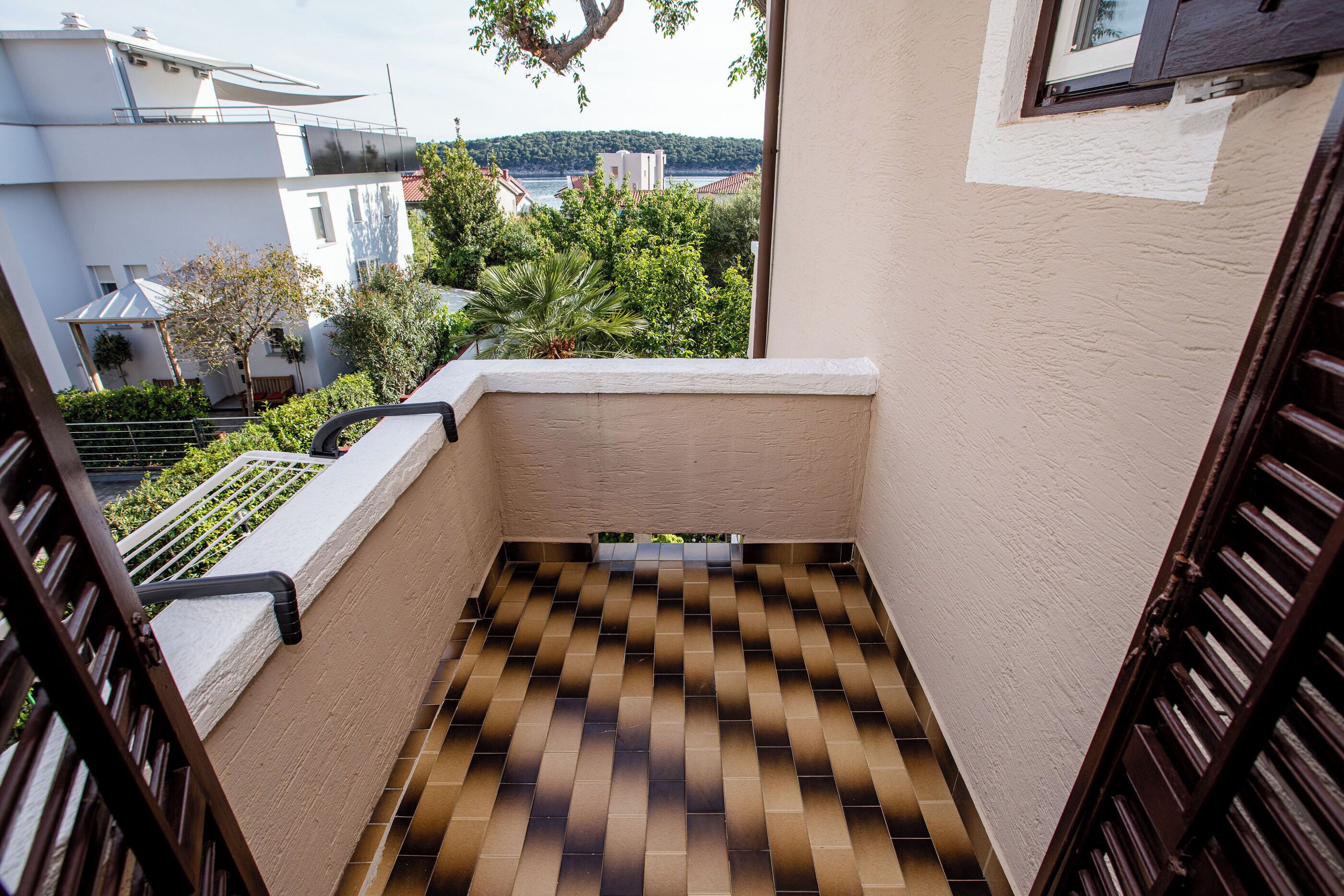 A balcony with a checkered floor, a view of buildings and trees, and a door with a wooden frame.