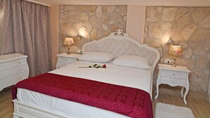 A bedroom with a stone wall, a white bed with a red bedspread, two bedside tables with lamps, and a modern ceiling light fixture. - House Star 1 (Dubrovnik)