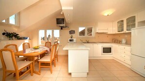 A modern kitchen with white cabinetry, a central island, and a dining area with wooden chairs and a table. - House Star 1 (Dubrovnik)