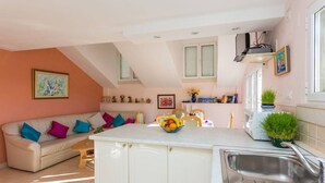 A modern kitchen with a central island, a dining area with a sofa, and a kitchen counter with plants. - House Star 1 (Dubrovnik)