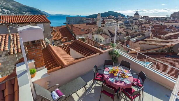 A rooftop terrace with a table set for dining, overlooking a coastal cityscape with terracotta rooftops and historic buildings. - House Star 1 (Dubrovnik)