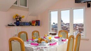 A dining area with a table set for four, a vase with flowers, and a city view through large windows. - House Star 1 (Dubrovnik)