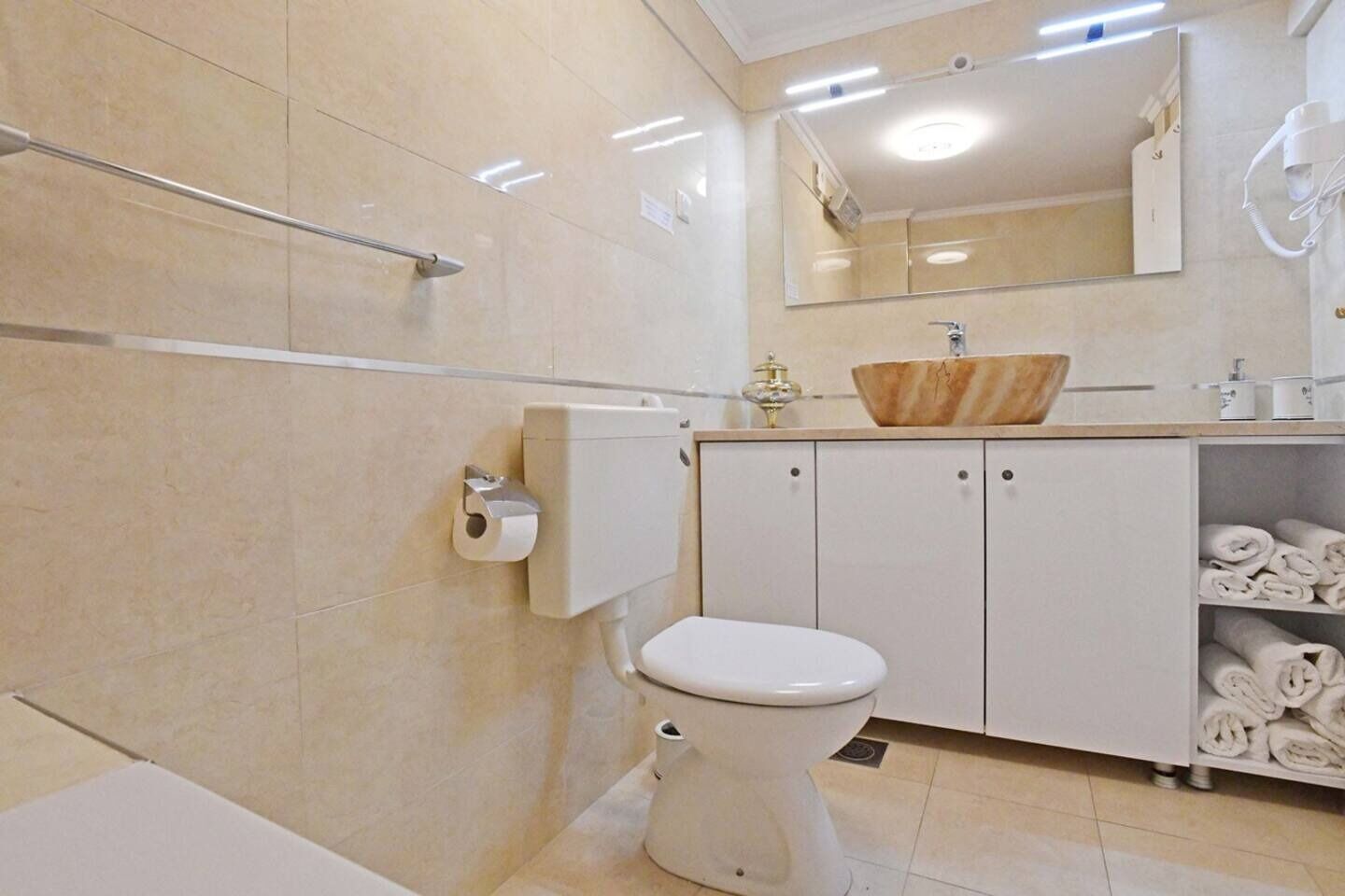 A modern bathroom with a toilet, a sink with a wooden basin, a towel rack, and a mirror.