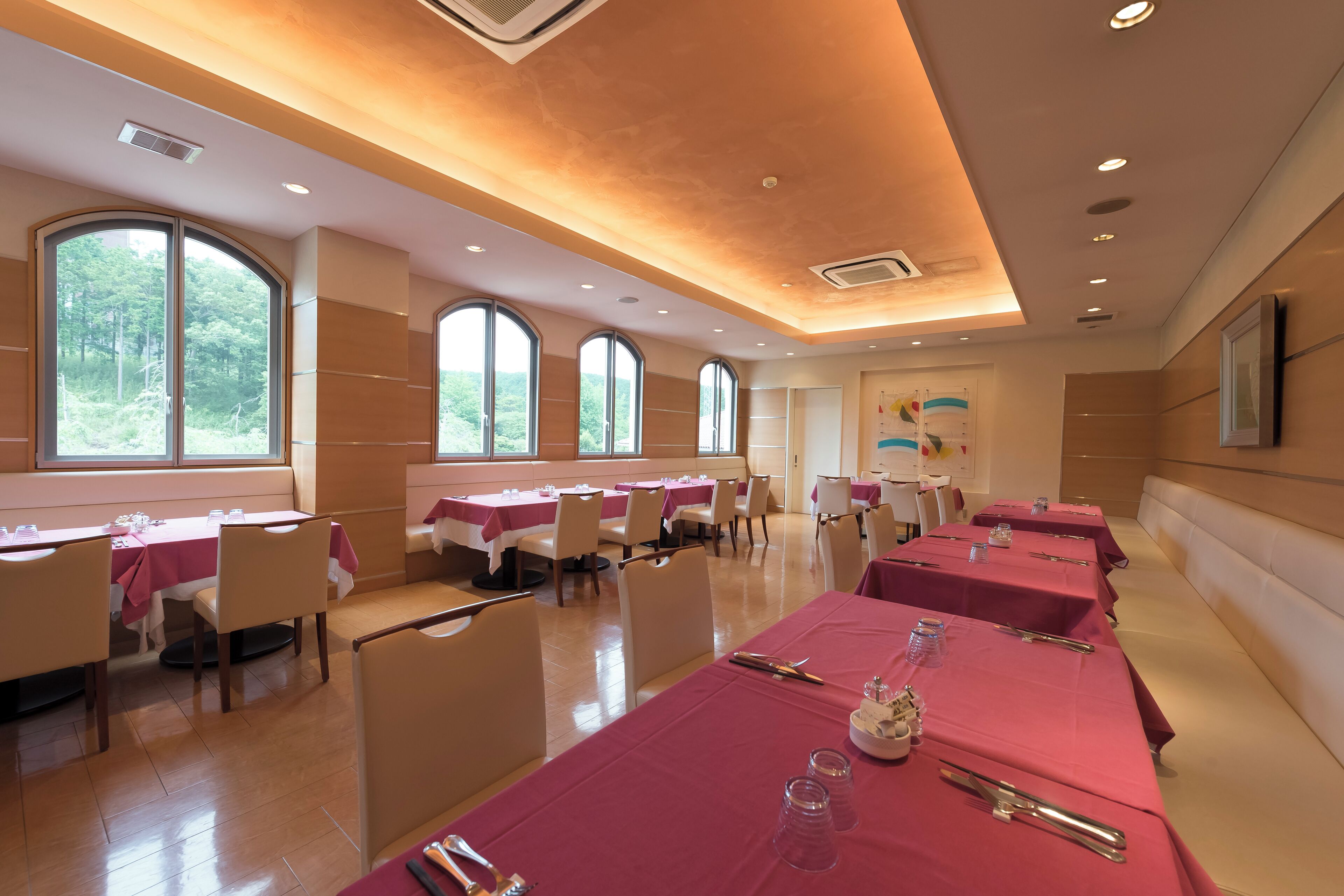A dining area with tables set for meals, large windows, and a modern ceiling design.