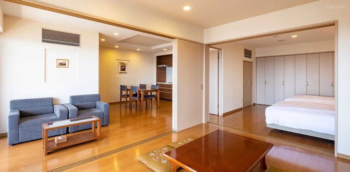 A modern hotel room with a wooden floor, a sofa, a dining table, and a large bed.