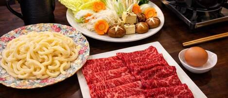 Une table avec une assiette de nouilles, une assiette de tranches de bœuf, un bol d’œufs et une théière.