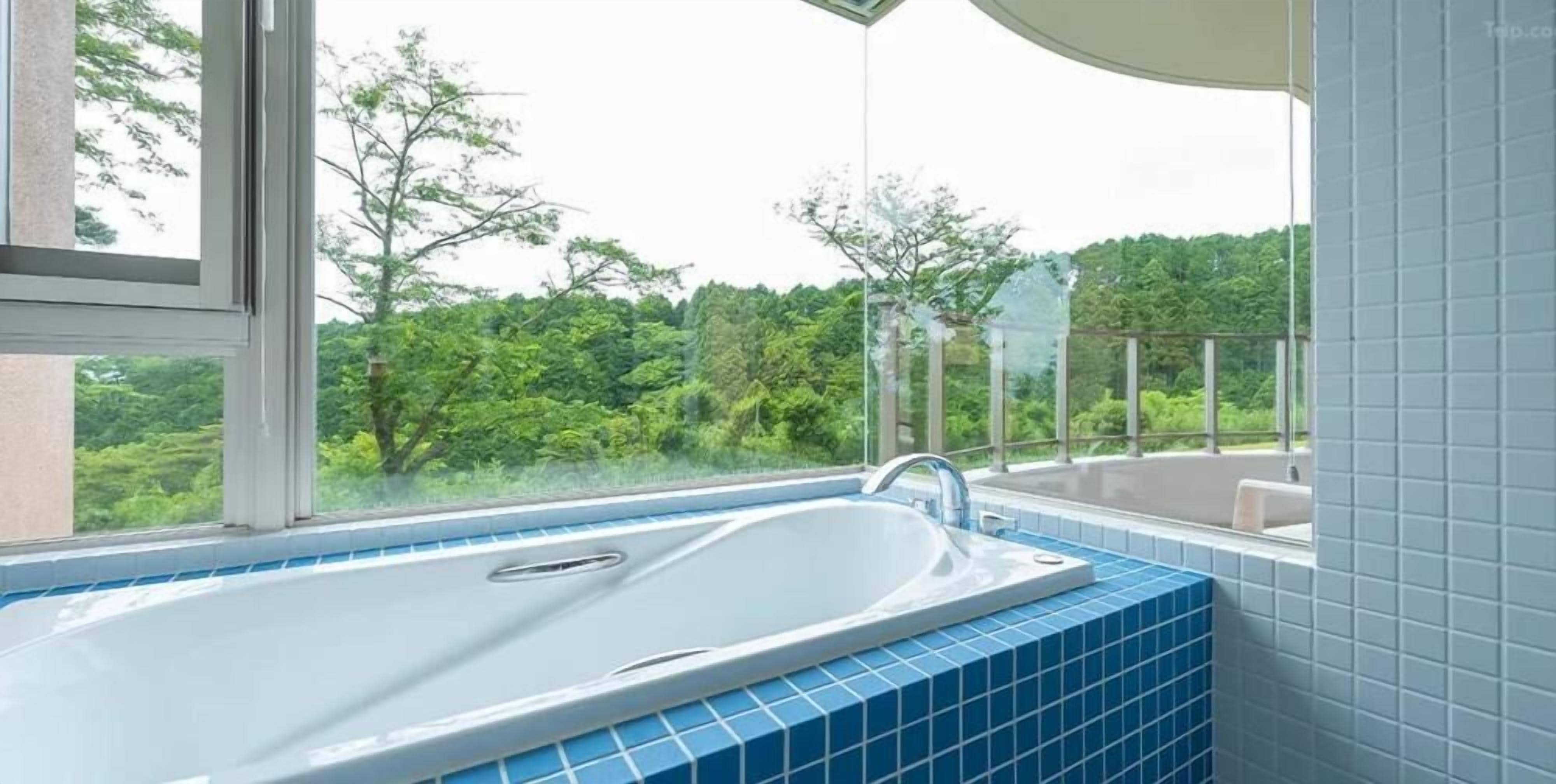 Un baño con bañera, ventana y vista a follaje.