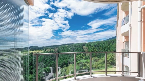 Un balcon doté d’une balustrade en verre, offrant une vue sur un paysage boisé.