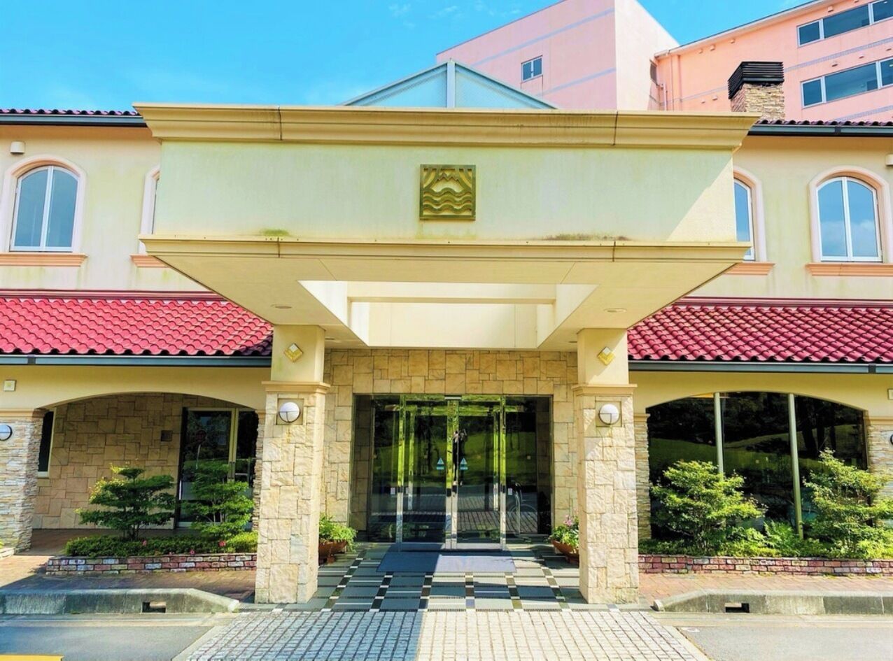 A hotel entrance with a glass door, stone pillars, and a red-tiled roof.