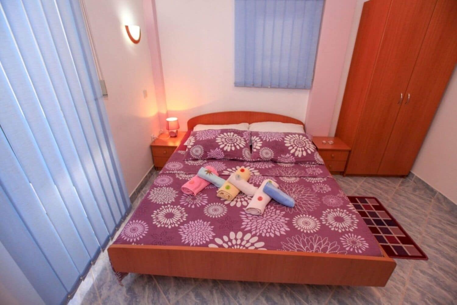Un dormitorio con cama, mesitas de noche, armario y ventana con persianas.