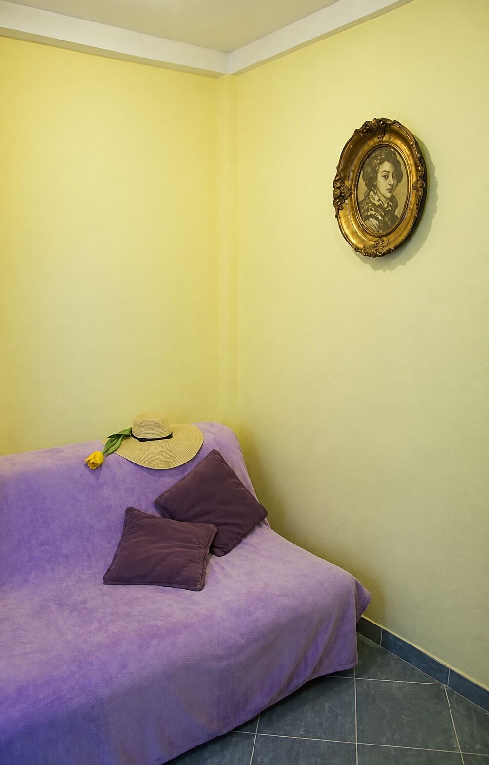 A room with a purple sofa, a hat, and a yellow flower on it.