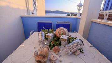 Uma mesa posta com conchas e recipientes de vidro numa varanda com vista para o mar.
