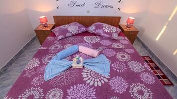 Een net opgemaakt bed met een bloemenprint sprei, twee kussens en een handdoekstapel op een betegelde vloer.