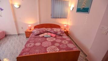 A bedroom with a bed, two bedside tables, a window with curtains, and a wall-mounted air conditioner.
