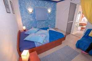 A bedroom with a bed, bedside lamps, a window with curtains, and a door leading to another room. - Apartments Drago (Slivno)