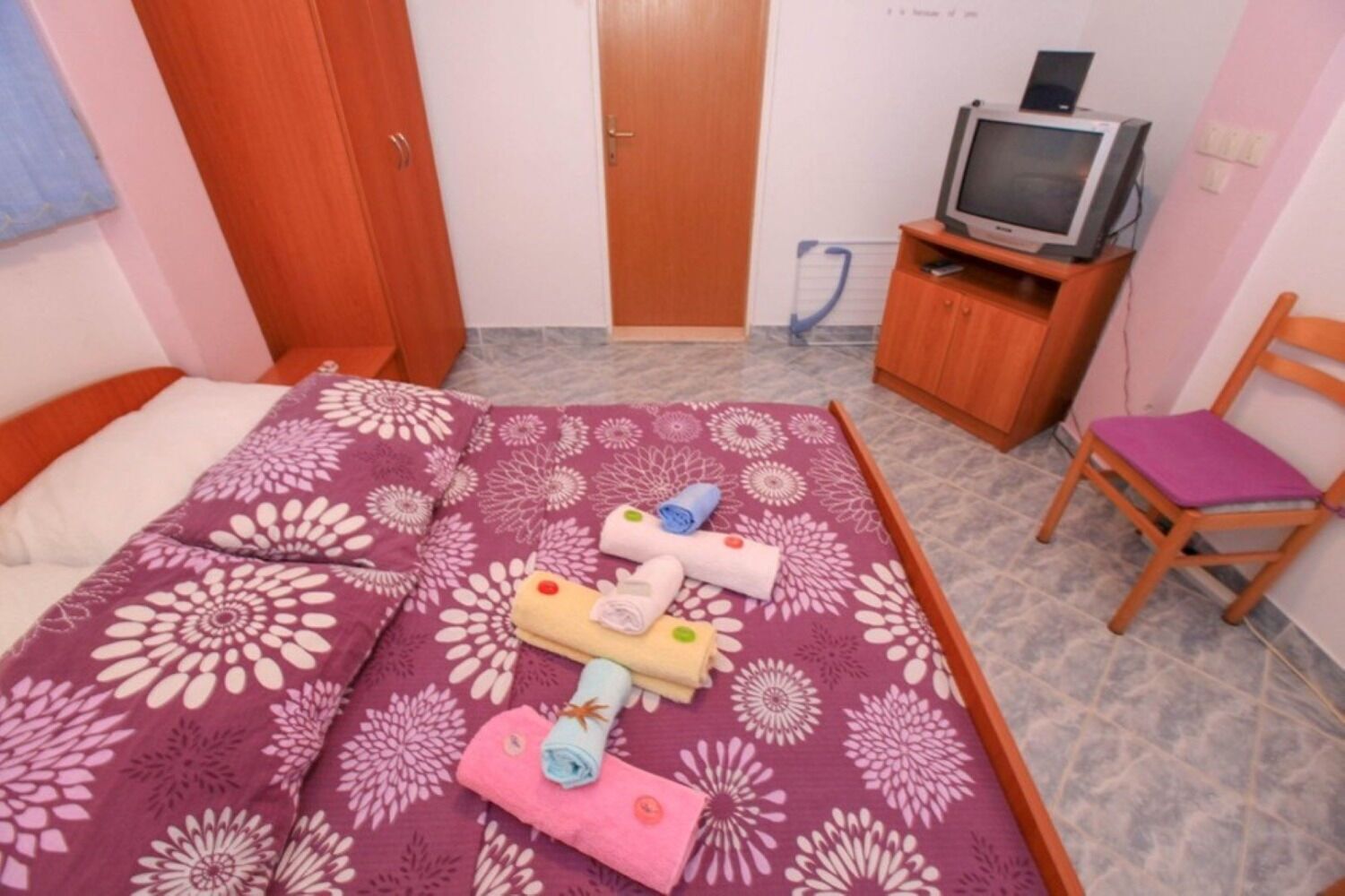 Un dormitorio con una cama, una silla de madera, un televisor y un armario.