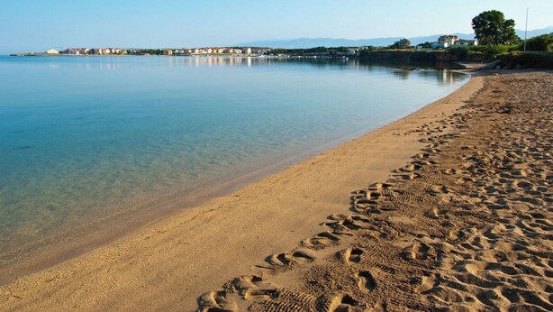 A beach with clear water, footprints, and buildings in the background. - Apartment San (Povljana)