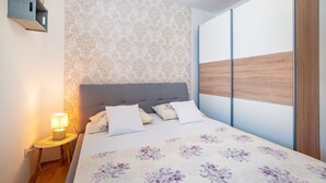 A bedroom with a bed, a nightstand with a lamp, a patterned wallpaper, and a wooden panel on the wall. - Apartment San (Povljana)