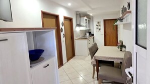 A compact kitchen with white cabinets, a blue bowl, a dining table with chairs, and a wooden door. - Apartment San (Povljana)