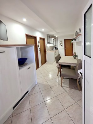 A compact kitchen with white cabinets, a blue bowl, a dining table with chairs, and a wooden door. - Apartment San (Povljana)