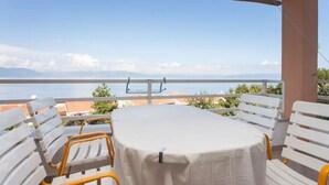 Ein Balkon mit Tisch und Stühlen, der auf ein Gewässer und eine entfernte Küste blickt.