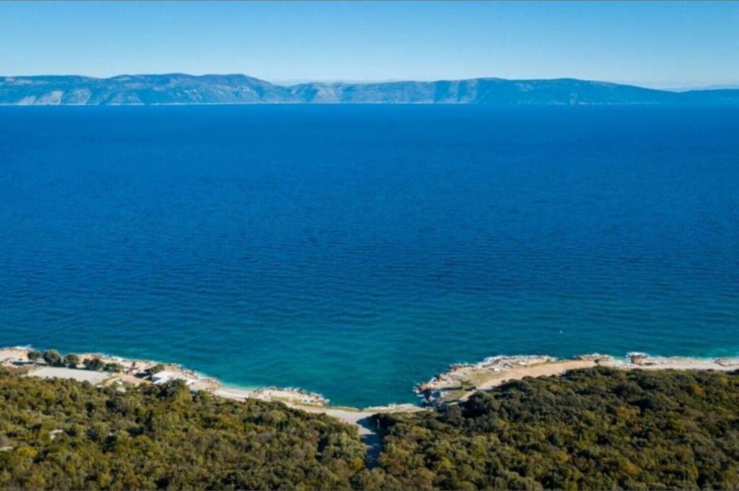 A coastal landscape with a clear view of the sea and distant mountains.