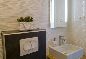 A modern bathroom with a dark vanity, a white sink, and a mirror above. - Apartment Marina (Korčula)