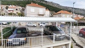 A parking area with cars, a covered walkway, and buildings in the background. - Apartment Anja (Dubrovnik)