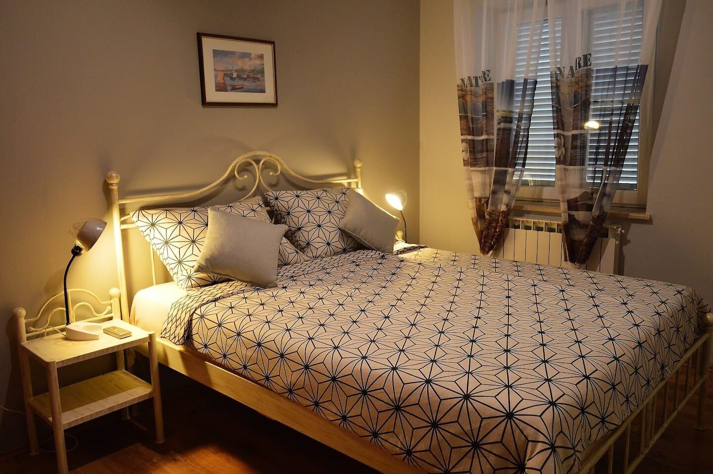 A neatly made bed with a geometric patterned bedspread, a bedside table with a lamp, and a framed picture on the wall.