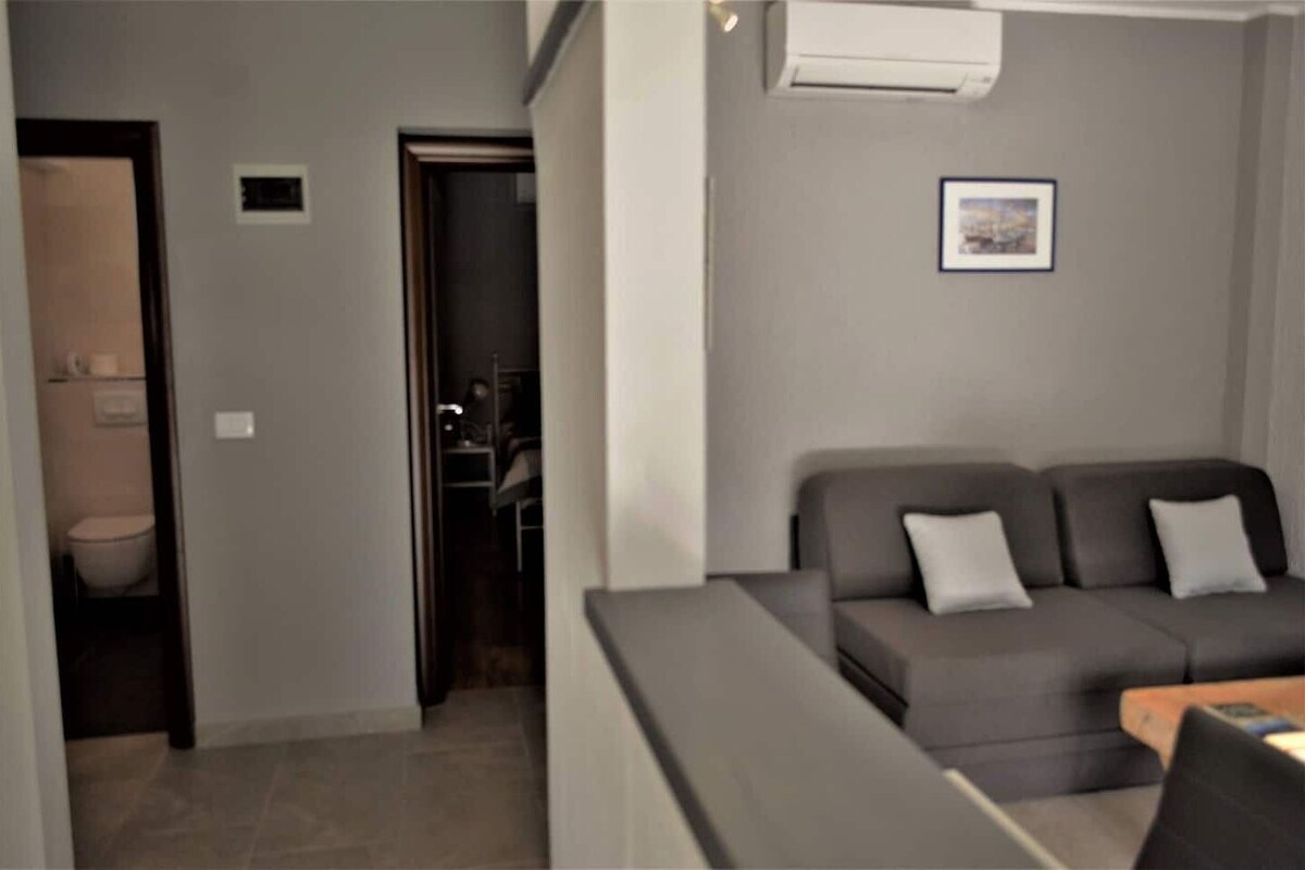 A living room with a grey sofa, a small table, and an air conditioning unit on the wall.