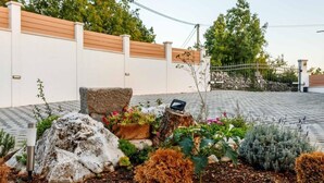 Un jardí paisatjistic amb una paret blanca, una tanca de fusta i una zona pavimentada.